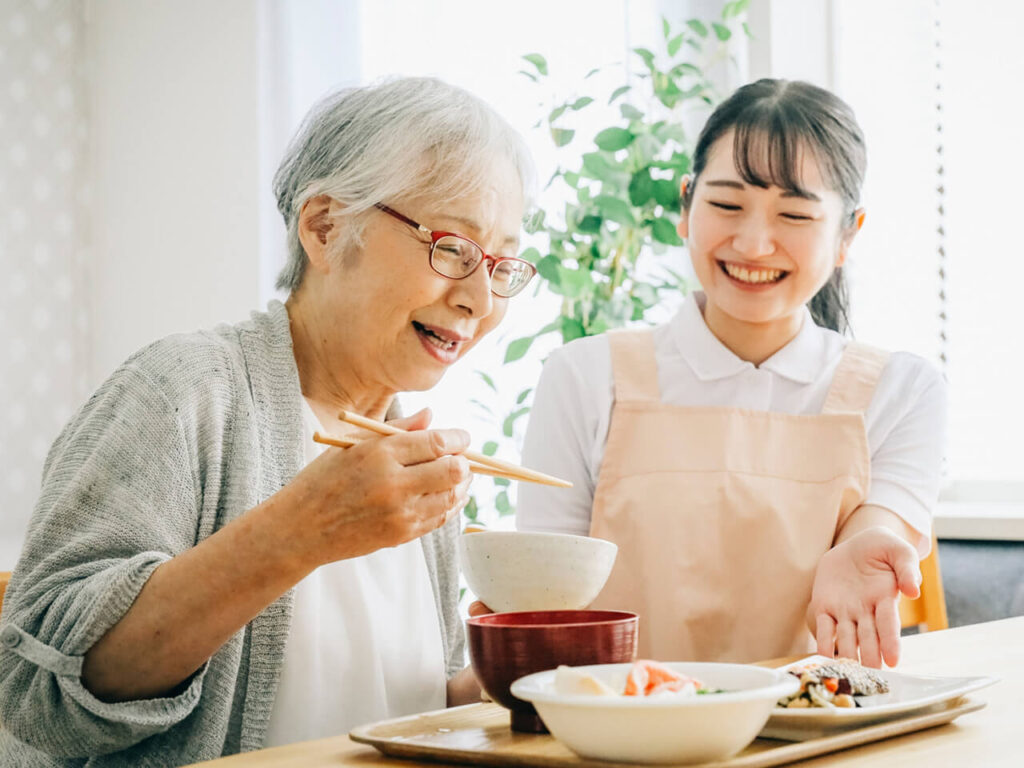 看護師が高齢女性と笑顔で食事の時間を過ごす様子