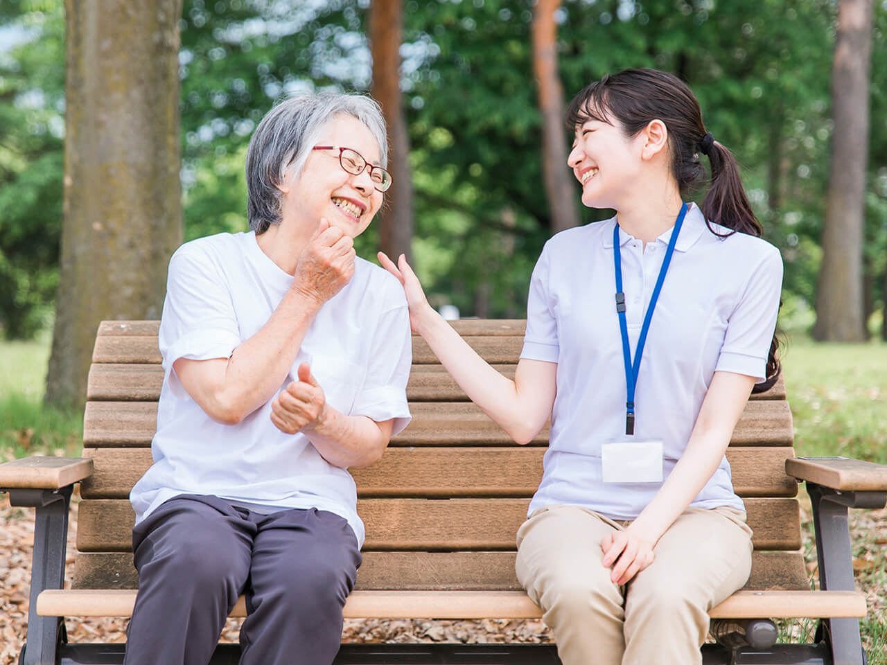 ベンチで看護師と高齢女性が笑顔で談笑する様子